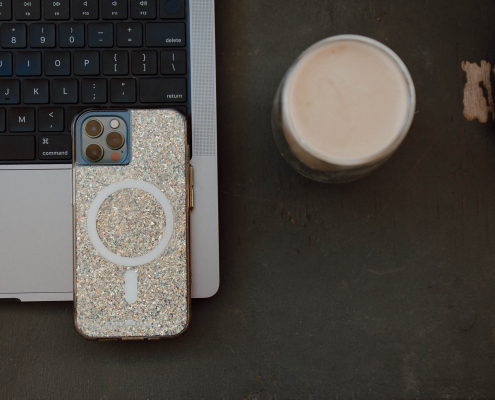Gold sparkly iPhone case facing upwards, place on a laptop with a latte beside on a concrete desk