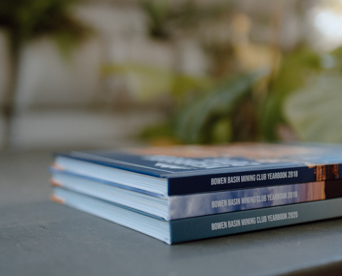 Three books stacked on each other, each a different yearbook from the Bowen Basic Mining Club 2018 - 2020
