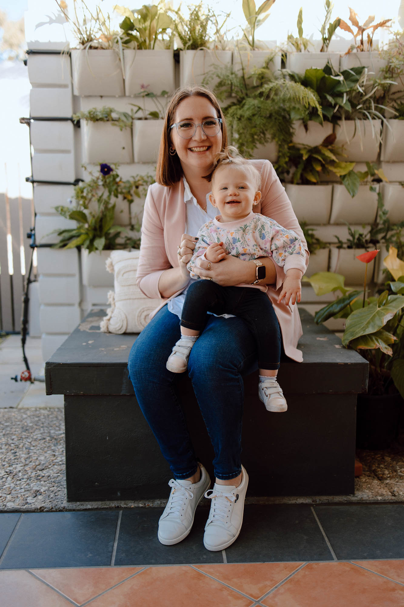 Sarah-Joy and her youngest daughter, smiling at the camera posed in front of a vertical garden